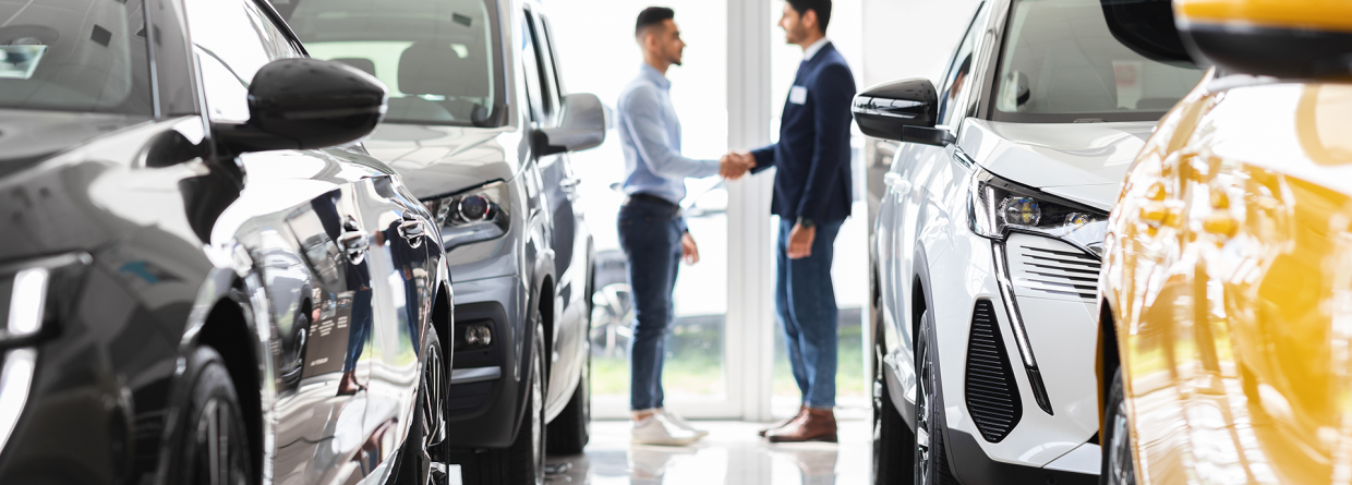 Auto lease; klant en verkoper schudden elkaar de hand in een showroom met auto's