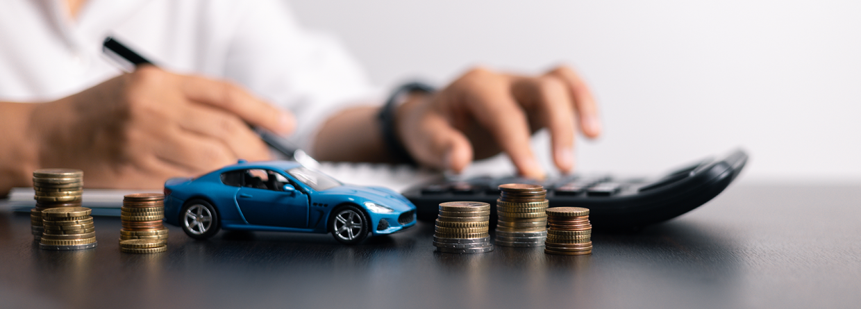 Man achter bureau met een pen, rekenmachine, miniatuur auto en stapels muntgeld