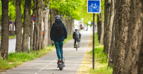 Een jongen op een elektrische step met een helm op en een rugtas