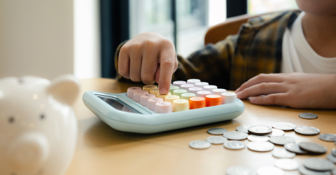 Kind telt muntgeld op rekenmachine uit spaarvarken